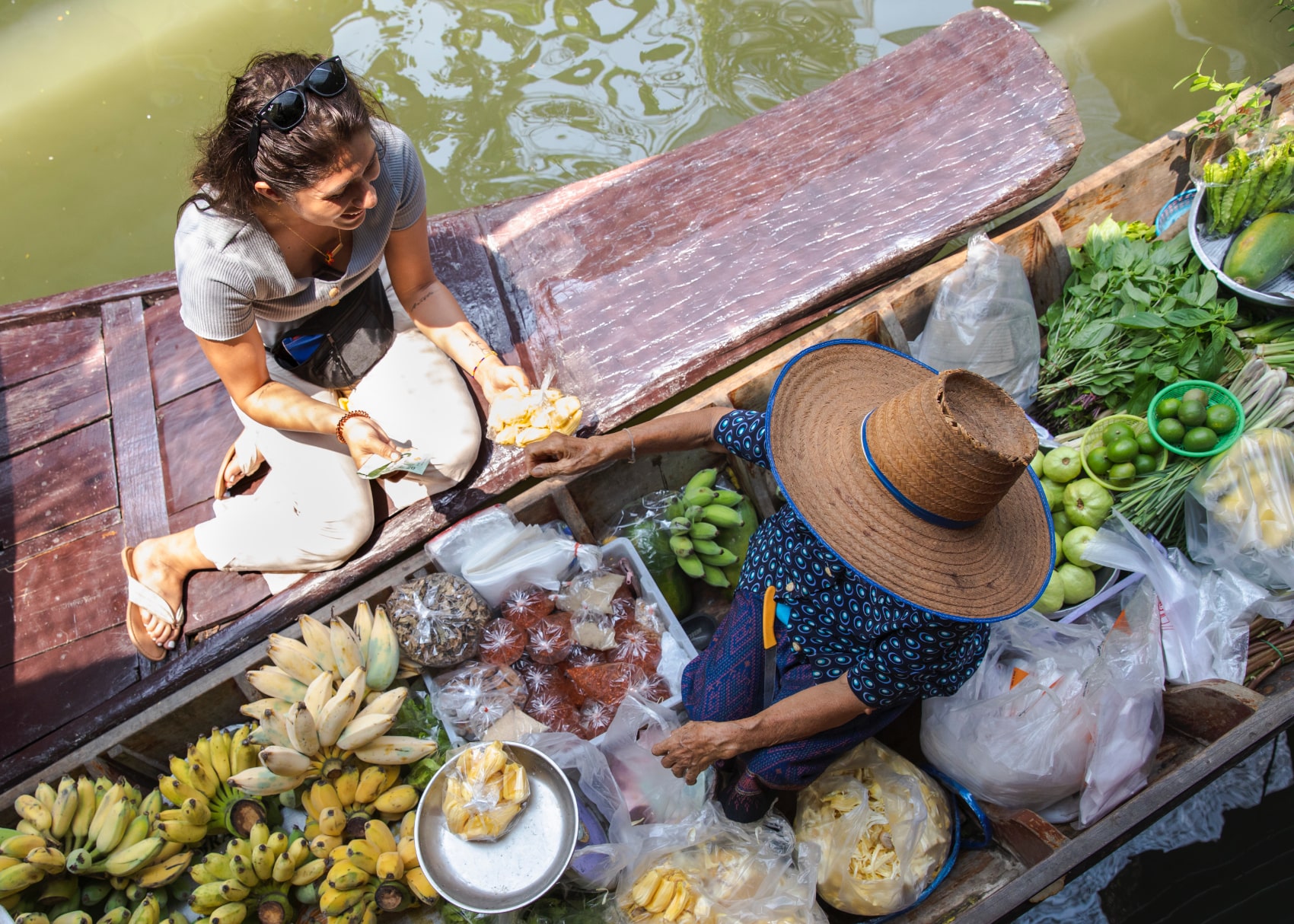 a traveller sits boatside in Thailand buying bananas from a vendor